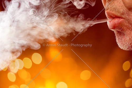 male mouth is blowing smoke out, with bokeh background