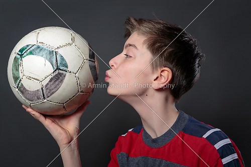 funny teenage boy is kissing a soccer ball, with gray background