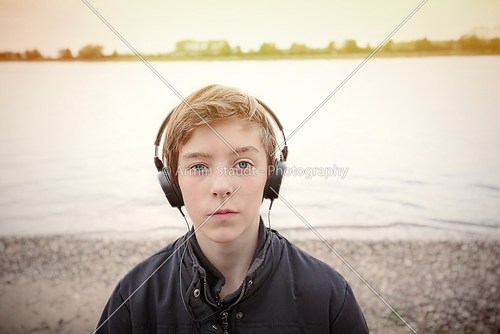 portrait of a teenage boy with headphones at a riverbank, toned 
