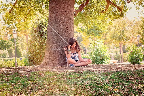 teenage girl is sitting and relaxing under a big tree in a park