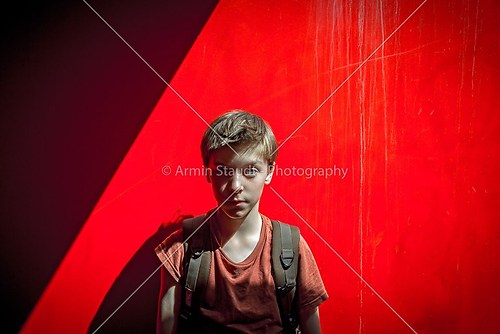 portrait of a teenager boy with rucksack in front of a red wall,