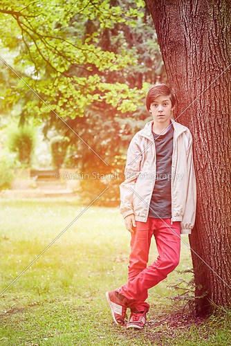 teenager boy leaning against a tree in a park