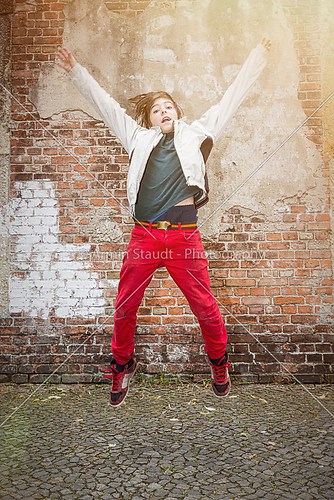 flying, jumping teenager boy in front of an old brick wall