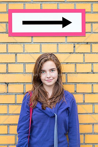 portrait of a female teenager standing under a direction sign wi