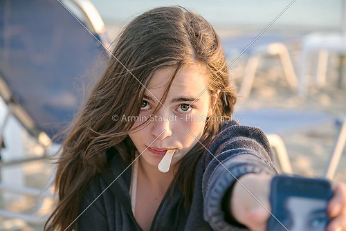 girl at the beach showing her self portrait on a smart phone 