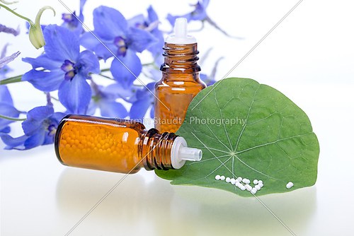 two bottles with homeopathy globules, green leaf and flowers