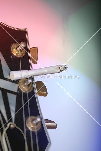 close up of a guitar headstock with burning cigarette sticking u