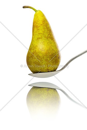 close up of a pear, standing on a spoon with reflection, isolate