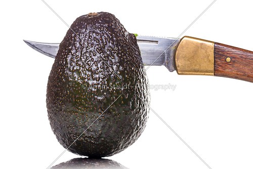 sharp knife  stings through an avocado, isolated on white
