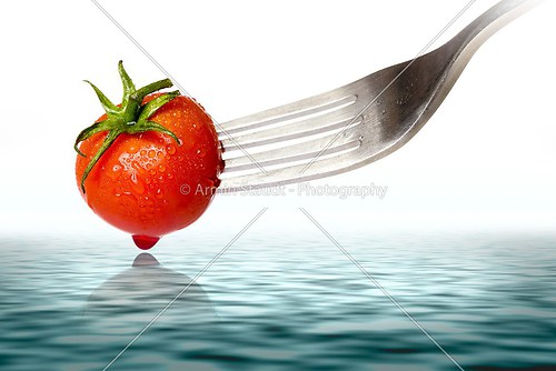 cherry tomato spiked by a fork with reflection in the ocean, iso