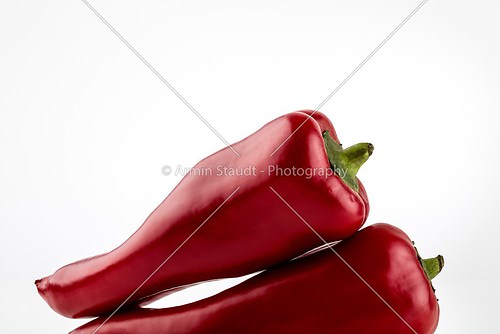 two red paprika are laying on each other, isolated on white
