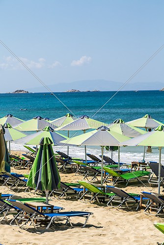 a group of green parasols and sun lounger with blue ocean in bac