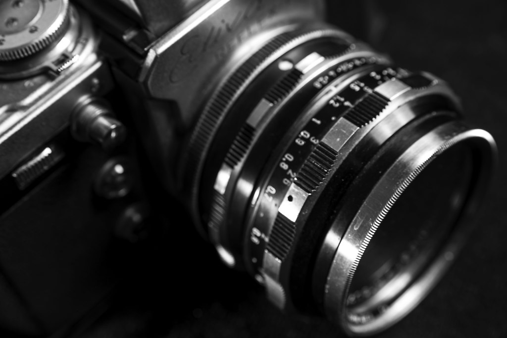 Photo Camera I (Photo Camera I) | Photo Camera I close-up black and white high angle view | camera, lens, close-up, black and white, no people, vintage, high angle view, technology, aperture, equipment, analogue, optics, old, studio, instrument, retro