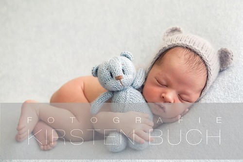 Newborn boy in a naked hat lies on a light blanket with a blue knitted bear (baby2)